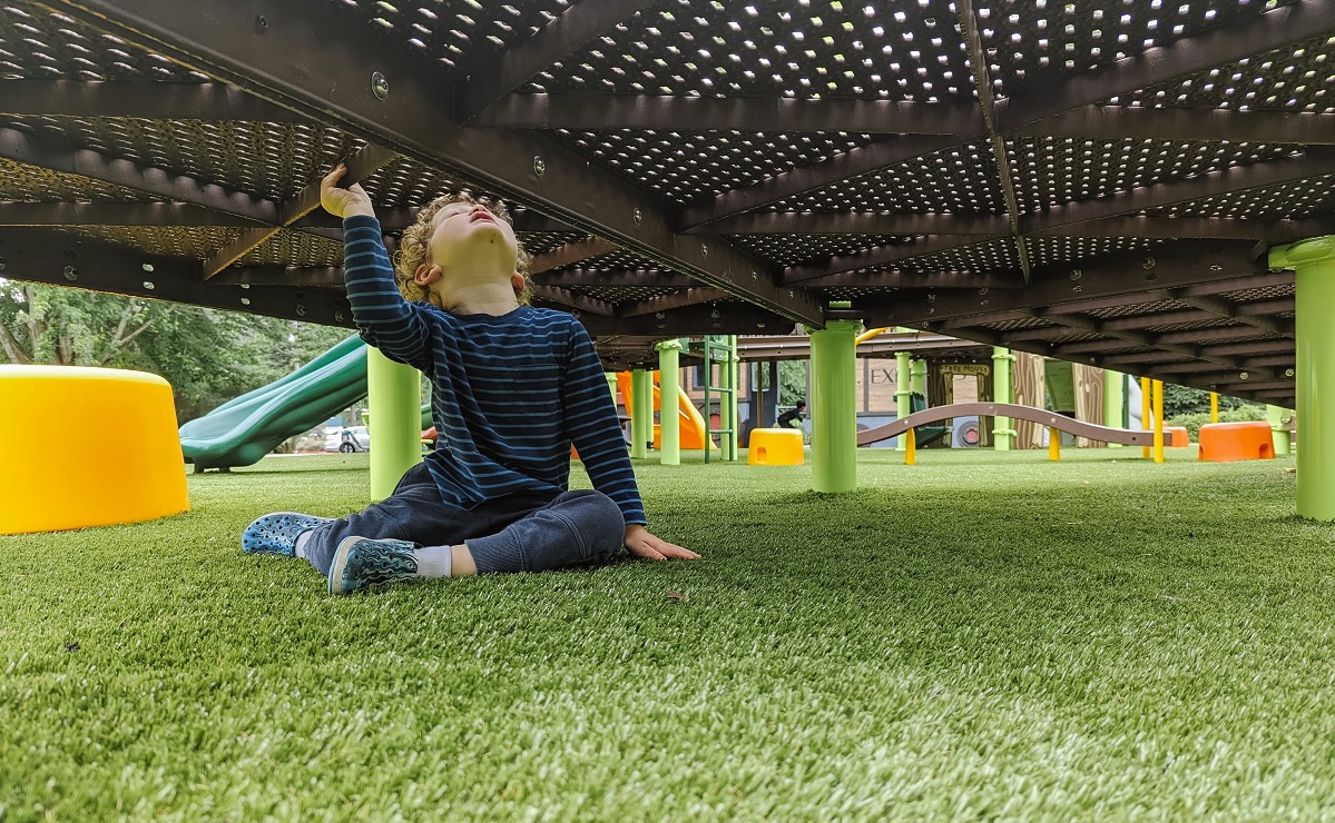 A young boy takes a quiet moment underneath the climbing structure at the new Train Park playground at Mercer Island’s Mercerdale Park near Seattle